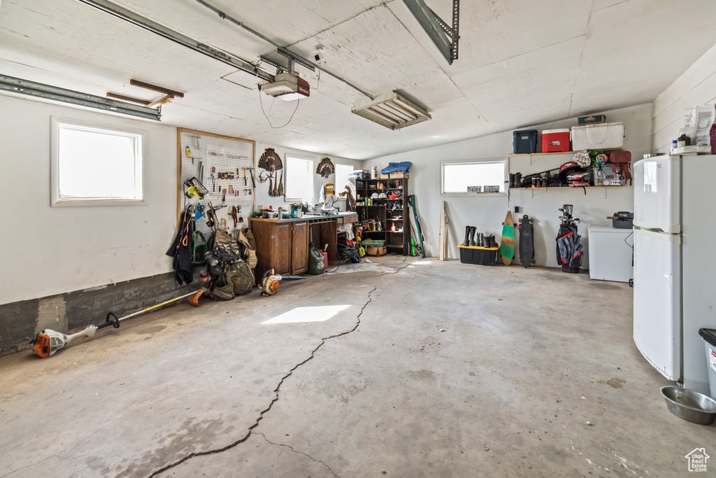 Garage with a garage door opener, a workshop area, and white refrigerator