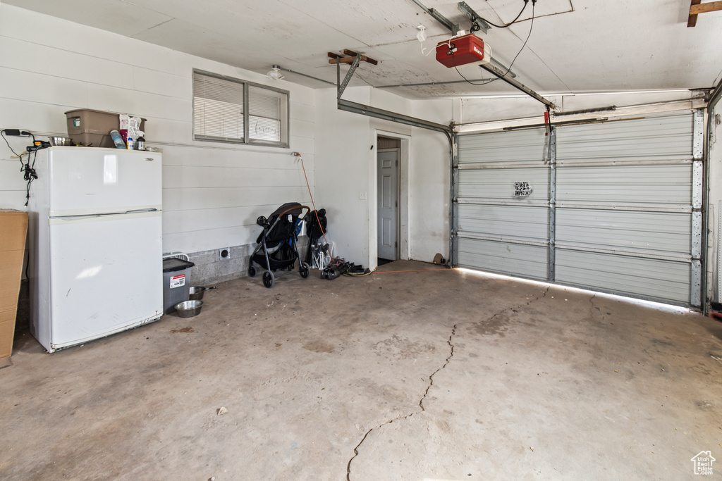 Garage featuring a garage door opener and white fridge