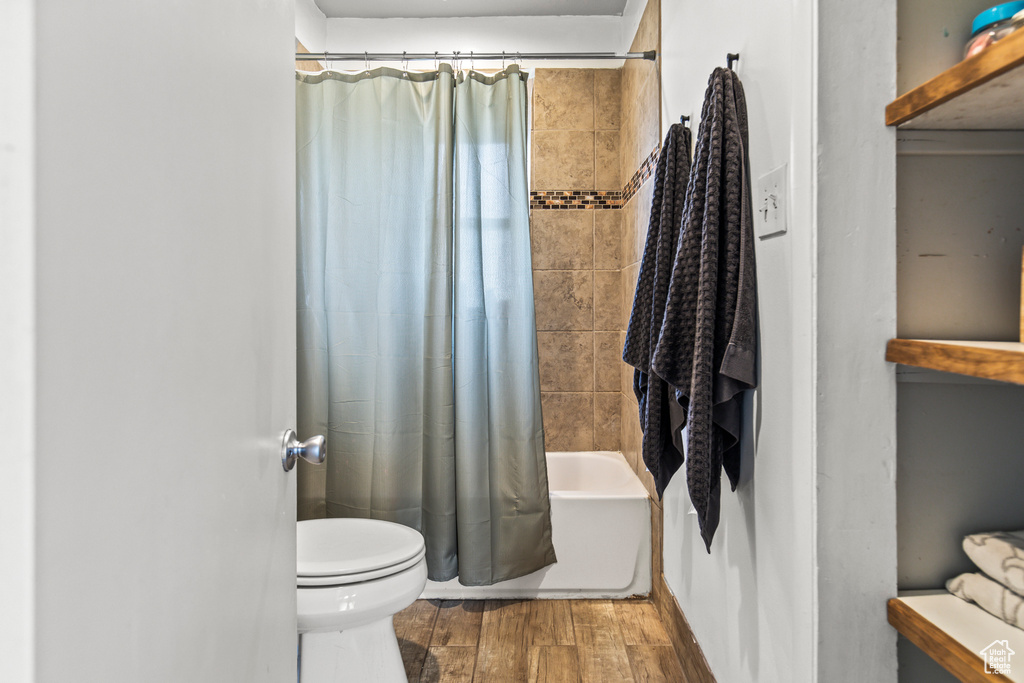 Bathroom with shower / tub combo with curtain, hardwood / wood-style floors, and toilet