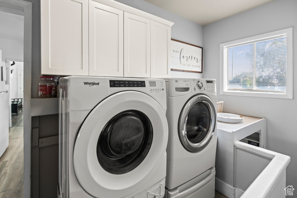 Laundry room featuring light hardwood / wood-style floors, washer and dryer, and cabinets