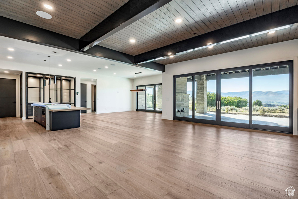 Unfurnished living room featuring a mountain view, beam ceiling, light hardwood / wood-style floors, and wooden ceiling