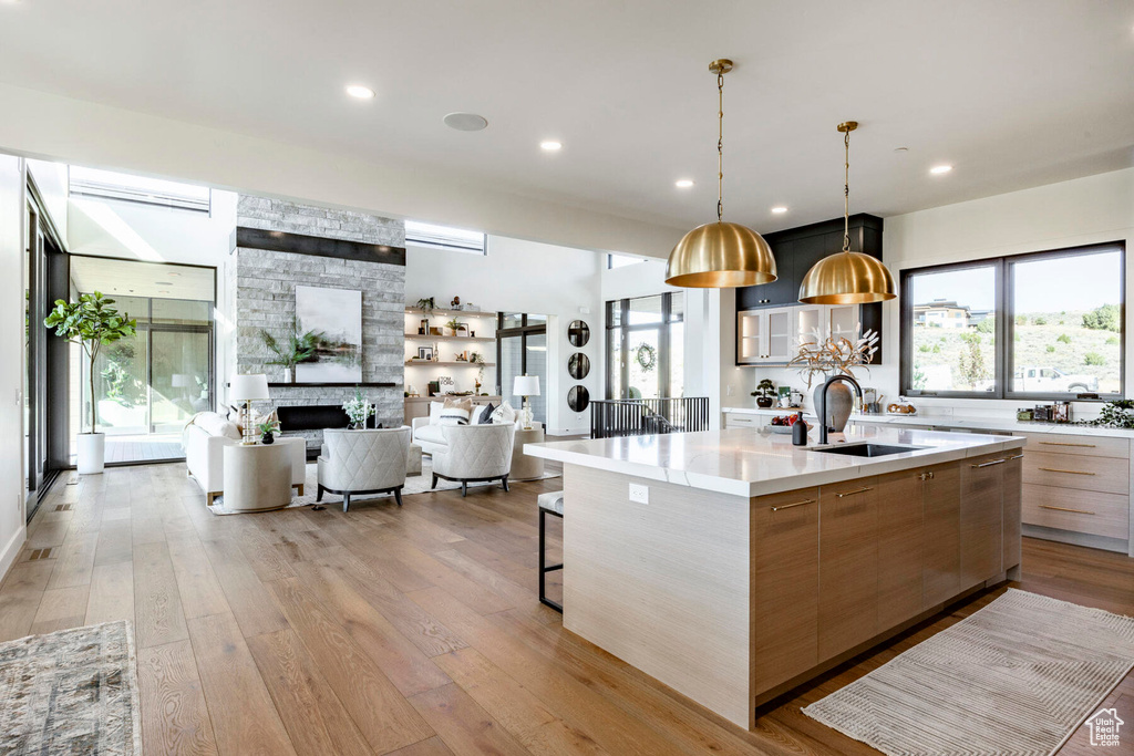 Kitchen with pendant lighting, sink, a stone fireplace, a large island with sink, and light wood-type flooring