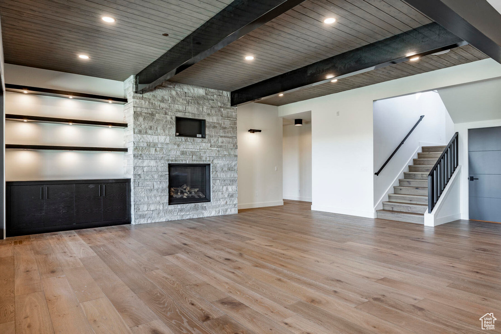 Unfurnished living room with light wood-type flooring, beam ceiling, wooden ceiling, and a stone fireplace