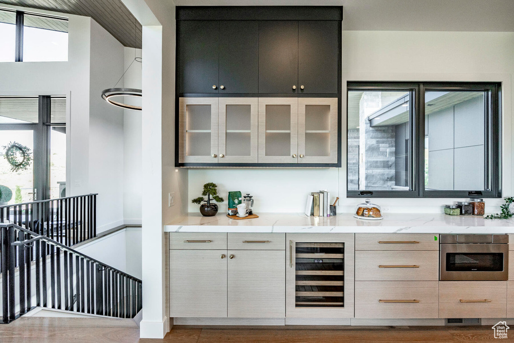 Bar featuring light hardwood / wood-style floors, light stone countertops, oven, and wine cooler