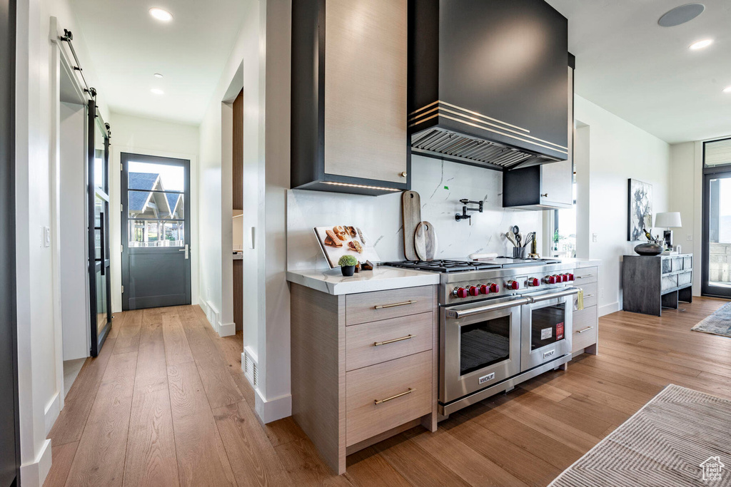 Kitchen featuring light brown cabinets, premium range hood, light hardwood / wood-style flooring, range with two ovens, and a barn door