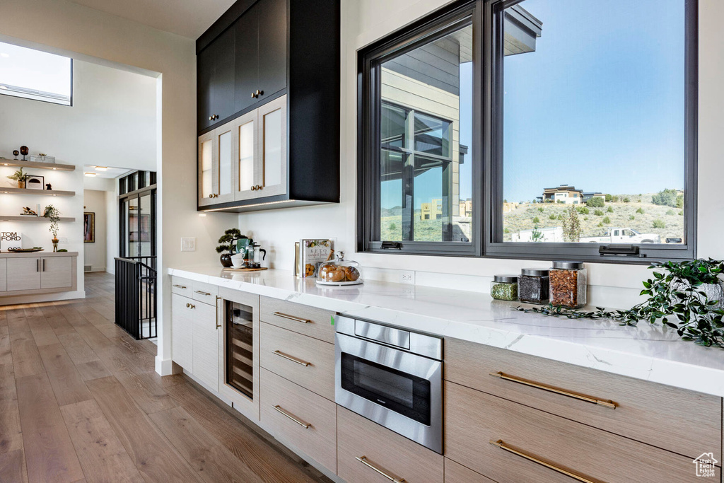 Kitchen featuring beverage cooler, light stone counters, light hardwood / wood-style floors, and light brown cabinetry