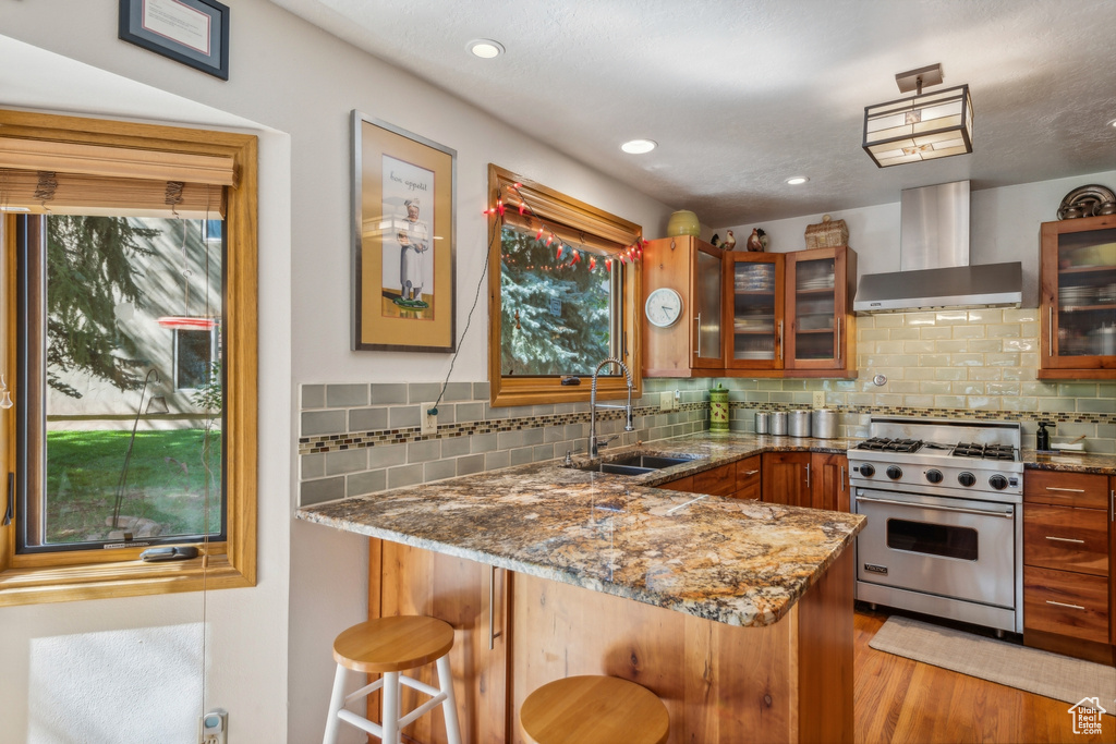 Kitchen with kitchen peninsula, designer range, light stone countertops, sink, and wall chimney range hood