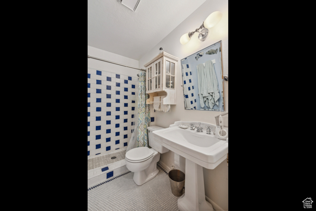 Bathroom with curtained shower, tile walls, tile patterned flooring, and toilet