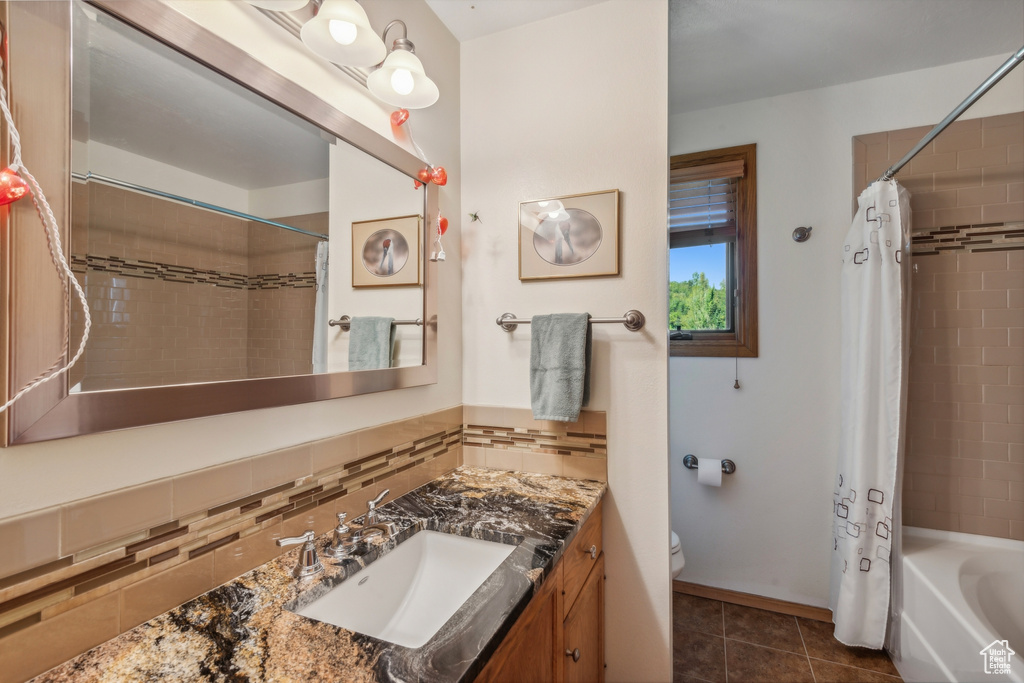 Full bathroom featuring decorative backsplash, shower / bathtub combination with curtain, vanity, tile patterned flooring, and toilet