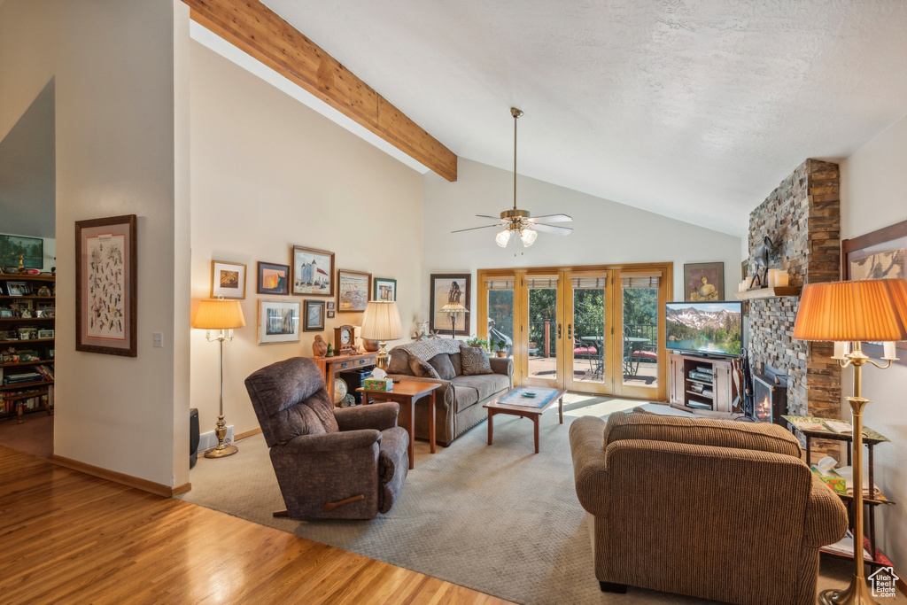 Living room with beamed ceiling, light hardwood / wood-style flooring, high vaulted ceiling, a stone fireplace, and ceiling fan