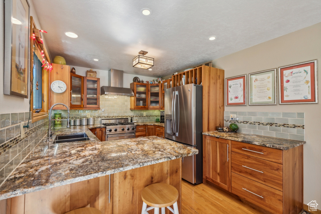 Kitchen featuring appliances with stainless steel finishes, kitchen peninsula, a kitchen bar, sink, and wall chimney range hood