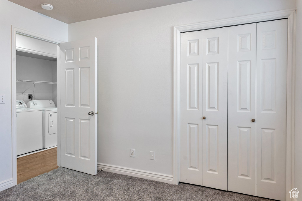 Unfurnished bedroom featuring light colored carpet, a closet, and washing machine and dryer