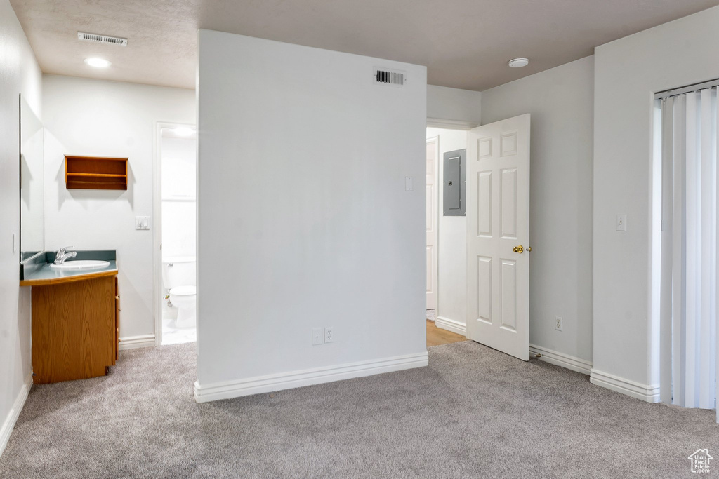 Unfurnished bedroom with electric panel, sink, light carpet, and ensuite bath