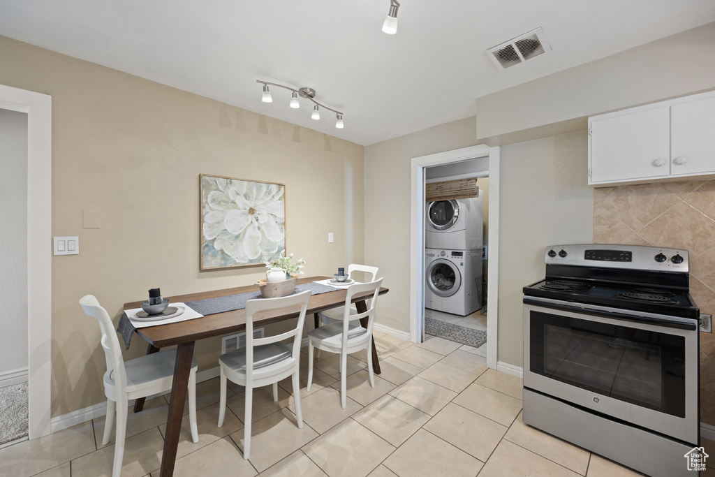 Kitchen with stacked washer and dryer, light tile patterned flooring, white cabinets, electric stove, and rail lighting