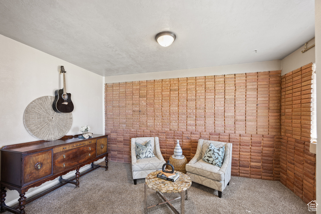 Living area featuring carpet, a textured ceiling, and brick wall