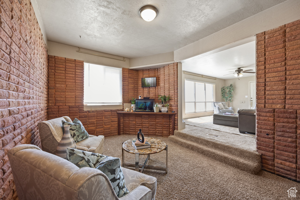 Living room featuring ceiling fan, brick wall, a textured ceiling, and carpet flooring