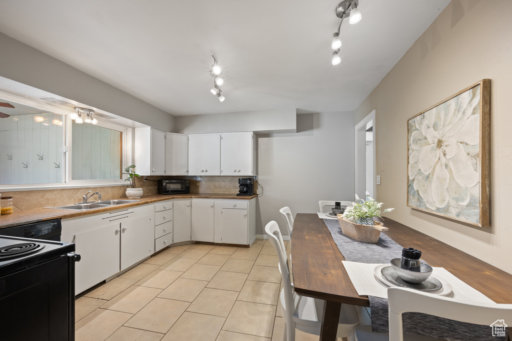 Kitchen with sink, white cabinets, rail lighting, black appliances, and backsplash