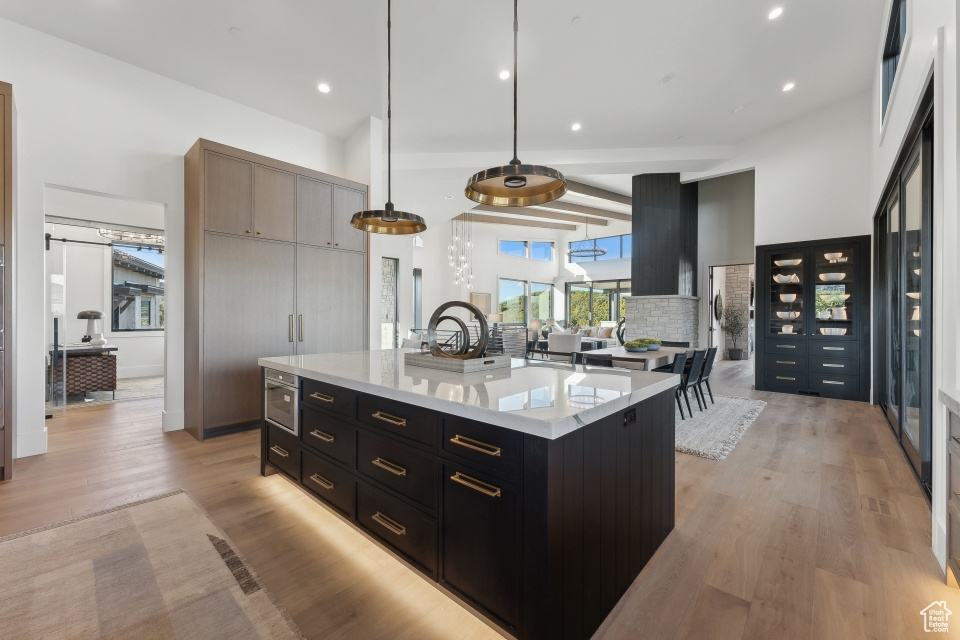 Kitchen with light stone counters, an island with sink, tasteful backsplash, pendant lighting, and light wood-type flooring