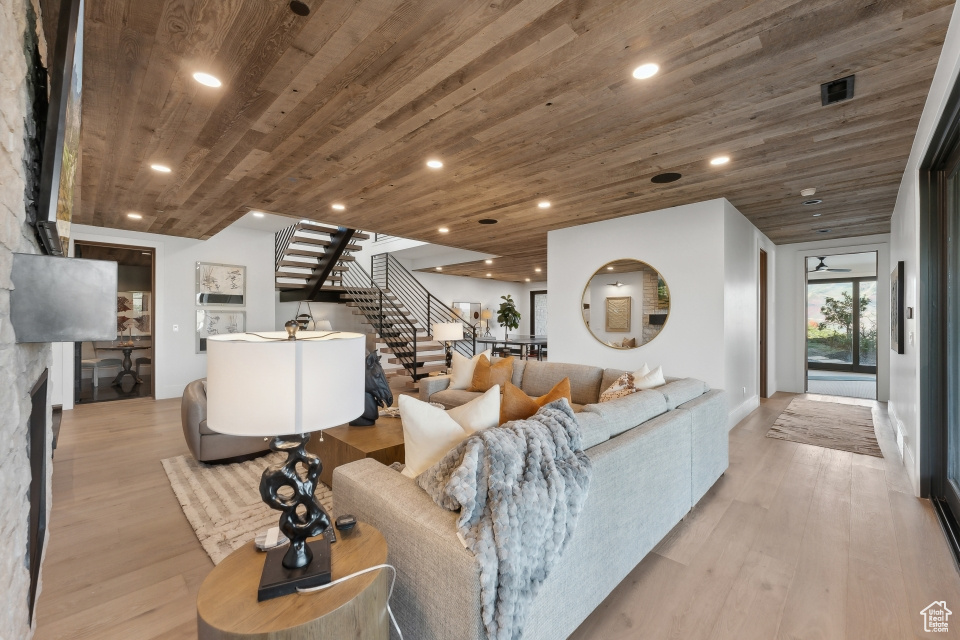 Living room with a stone fireplace, light hardwood / wood-style floors, and wooden ceiling