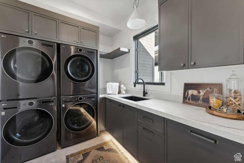 Clothes washing area featuring cabinets, sink, washing machine and dryer, and stacked washing maching and dryer