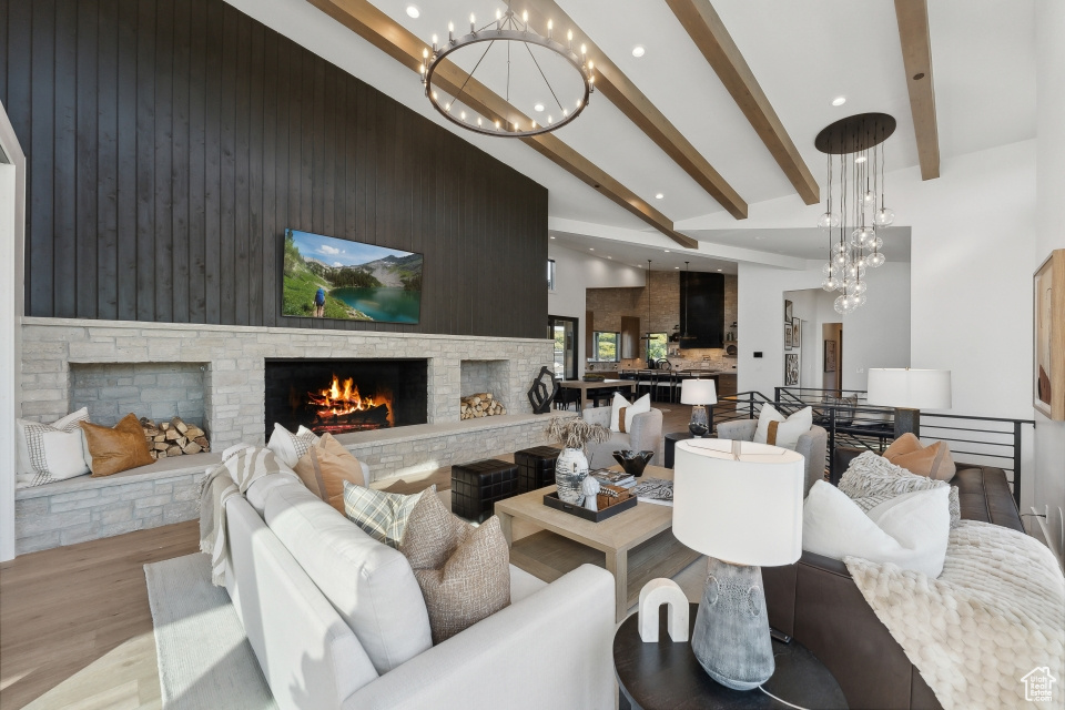 Living room featuring light wood-type flooring, a chandelier, beam ceiling, high vaulted ceiling, and a stone fireplace