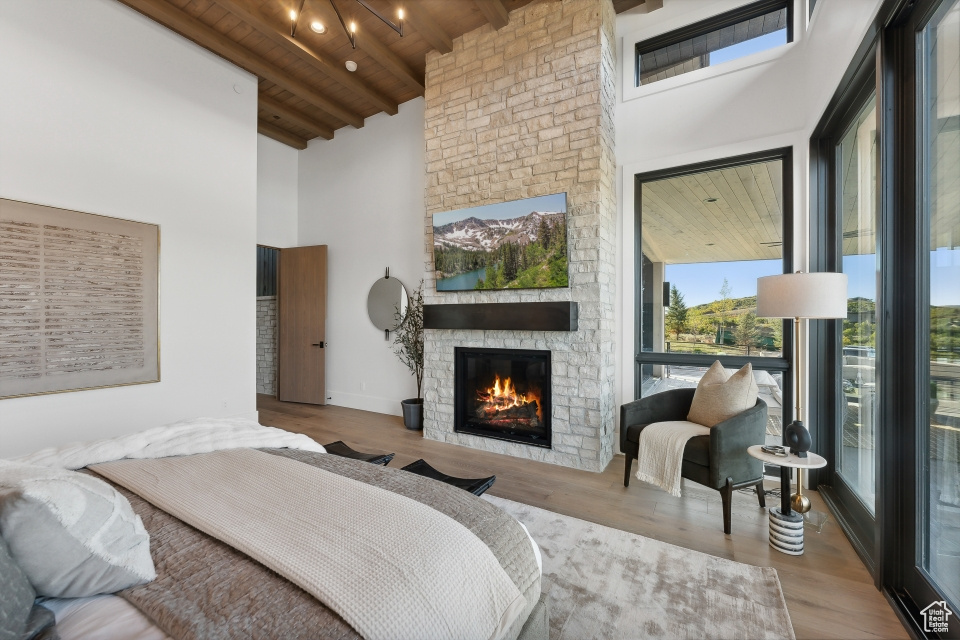 Bedroom featuring wood ceiling, light hardwood / wood-style floors, beam ceiling, a fireplace, and high vaulted ceiling