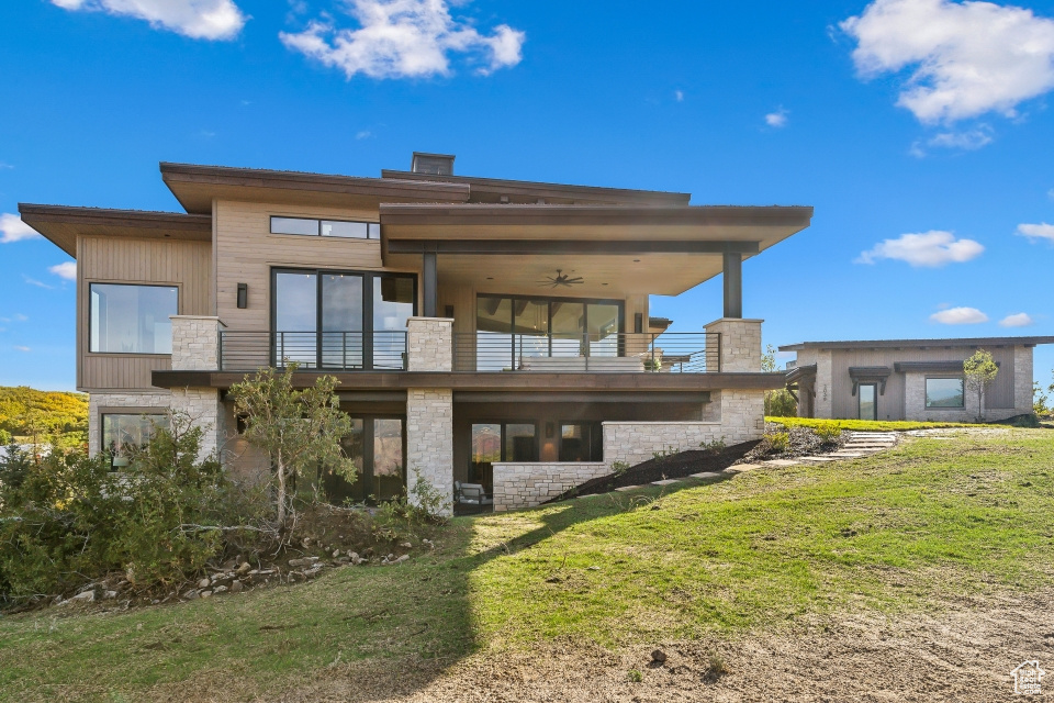 Rear view of property featuring ceiling fan, a balcony, and a lawn