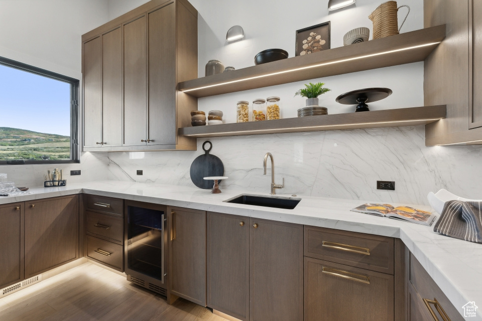 Kitchen with decorative backsplash, light stone countertops, light wood-type flooring, beverage cooler, and sink