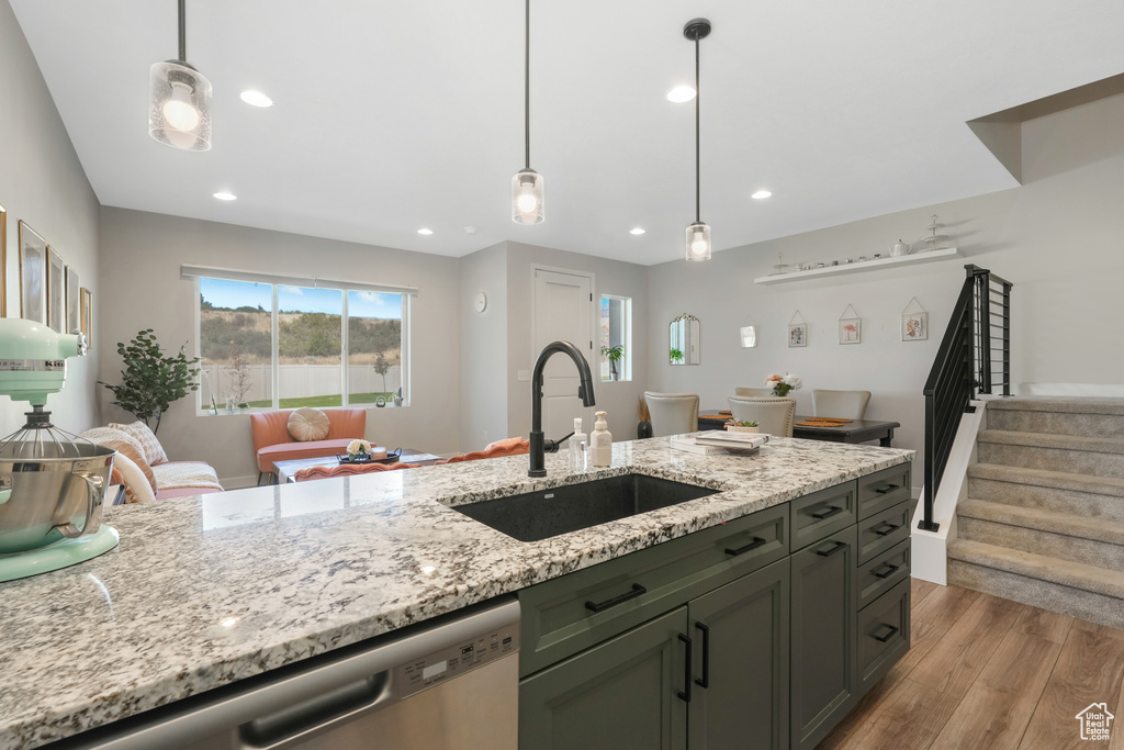 Kitchen with light wood-type flooring, sink, decorative light fixtures, light stone countertops, and stainless steel dishwasher