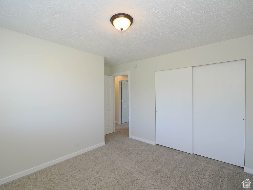 Unfurnished bedroom featuring light carpet, a closet, and a textured ceiling