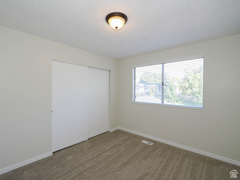 Unfurnished bedroom with a textured ceiling, a closet, and carpet flooring