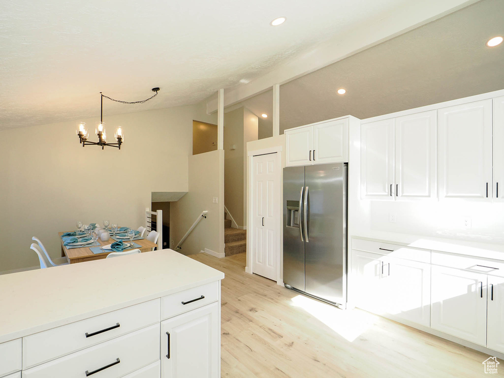 Kitchen featuring light hardwood / wood-style flooring, vaulted ceiling, white cabinetry, and stainless steel fridge