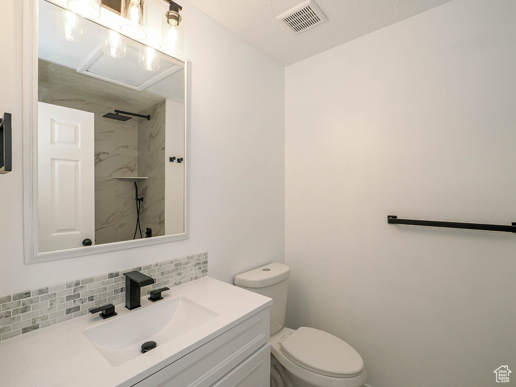 Bathroom with a tile shower, vanity, toilet, and decorative backsplash