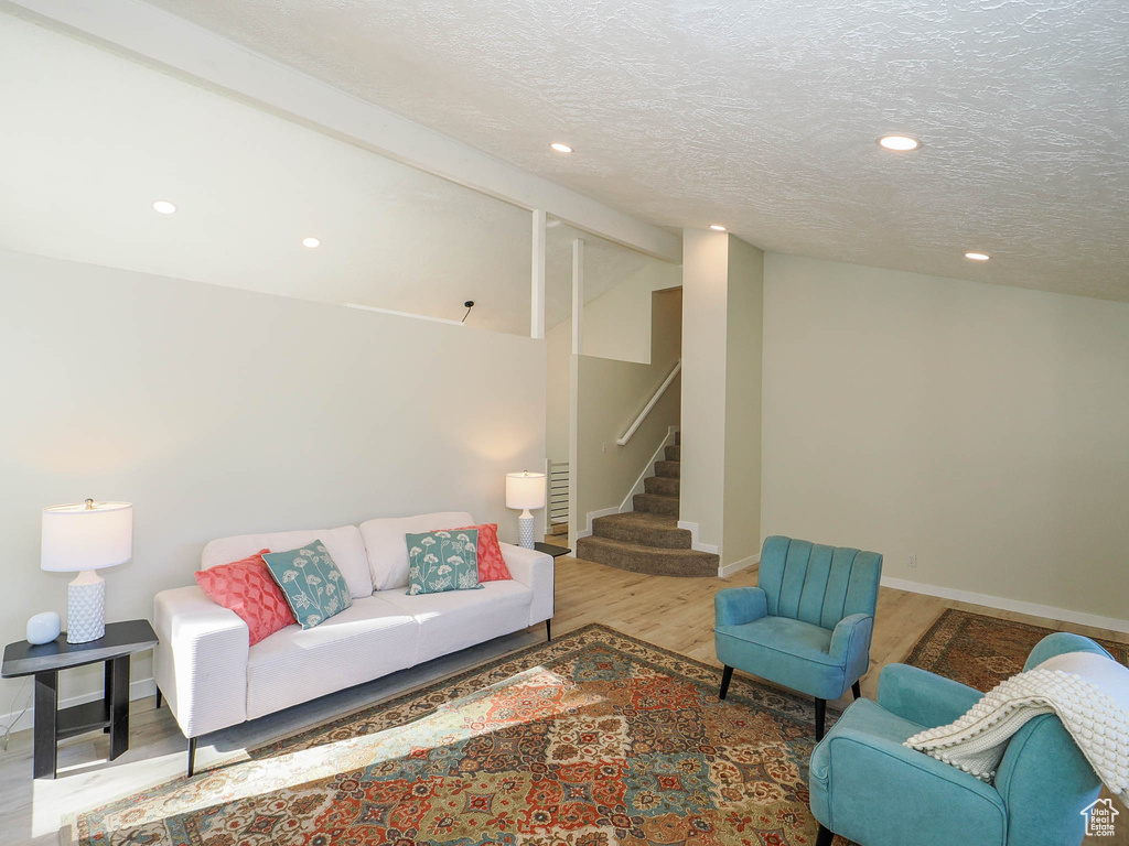 Living room with a textured ceiling, vaulted ceiling, and hardwood / wood-style flooring