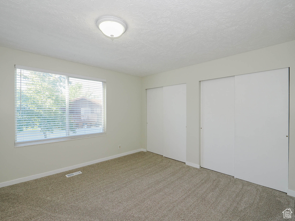 Unfurnished bedroom with multiple closets, a textured ceiling, and carpet flooring