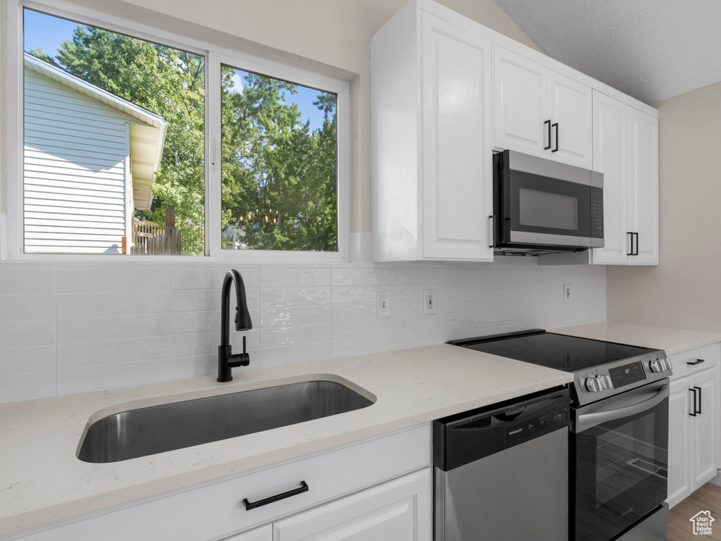 Kitchen with white cabinetry, stainless steel appliances, and light stone counters