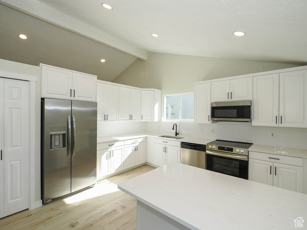 Kitchen with lofted ceiling with beams, sink, white cabinetry, light hardwood / wood-style flooring, and appliances with stainless steel finishes