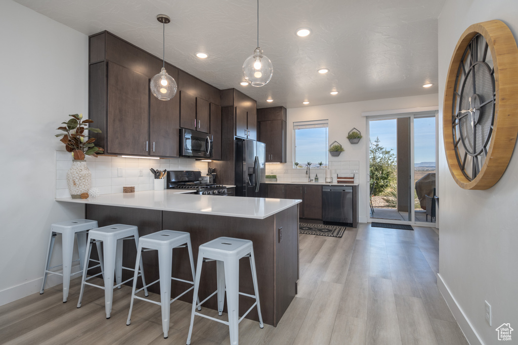 Kitchen featuring decorative backsplash, light hardwood / wood-style floors, kitchen peninsula, stainless steel appliances, and dark brown cabinets