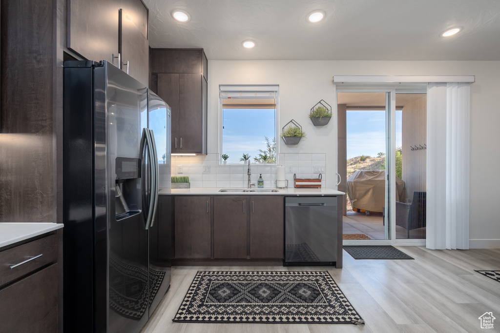 Kitchen with dark brown cabinets, light wood-type flooring, sink, backsplash, and appliances with stainless steel finishes