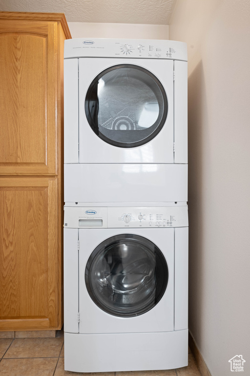 Washroom with cabinets, stacked washer and dryer, a textured ceiling, and light tile patterned floors