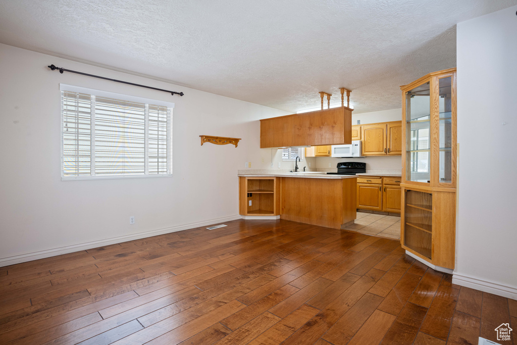 Kitchen featuring a textured ceiling, black stove, hardwood / wood-style floors, and kitchen peninsula