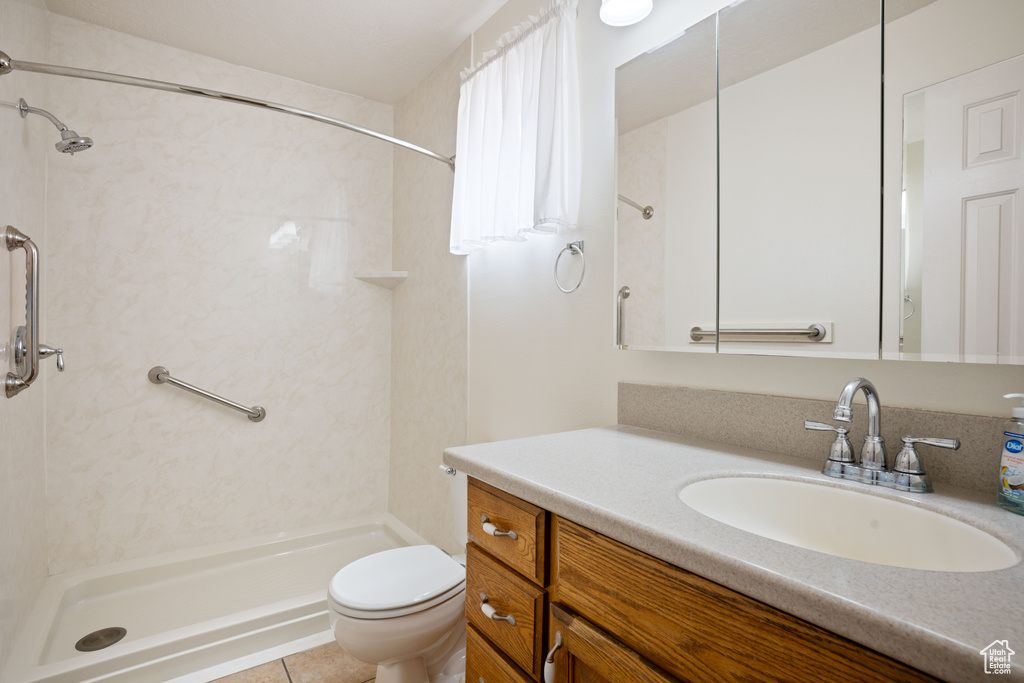 Bathroom with vanity, tile patterned flooring, toilet, and tiled shower