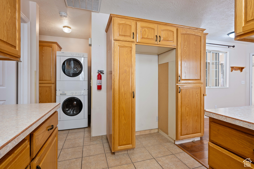 Kitchen with a textured ceiling, light tile patterned flooring, and stacked washer and clothes dryer