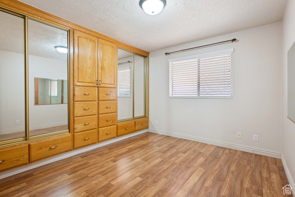 Unfurnished bedroom with a textured ceiling, a closet, and light hardwood / wood-style flooring