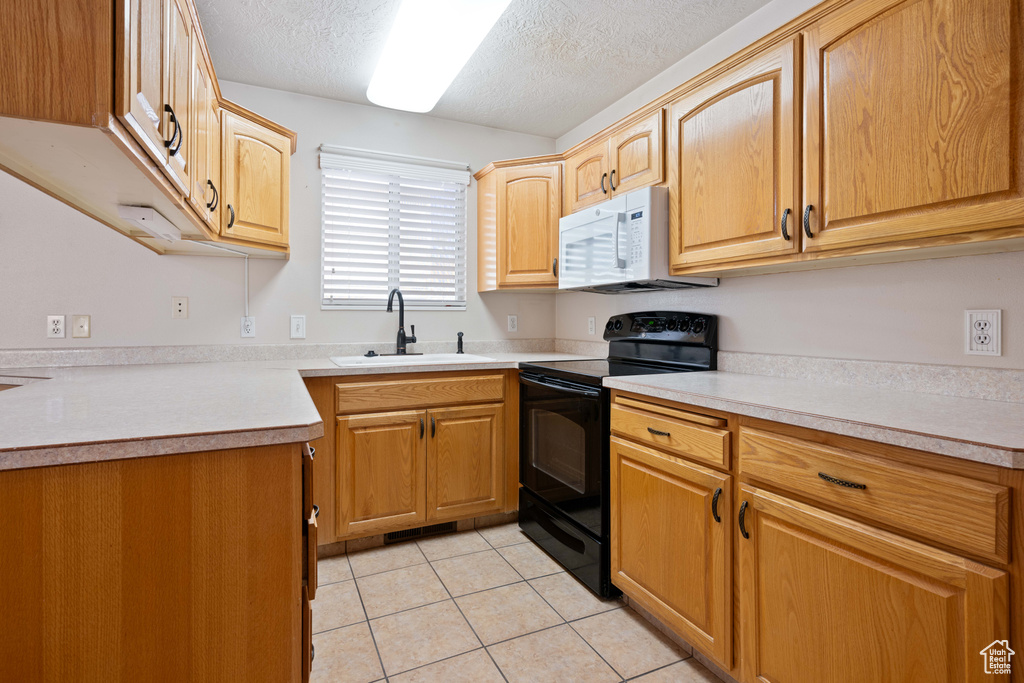 Kitchen with a textured ceiling, black electric range oven, sink, and light tile patterned floors