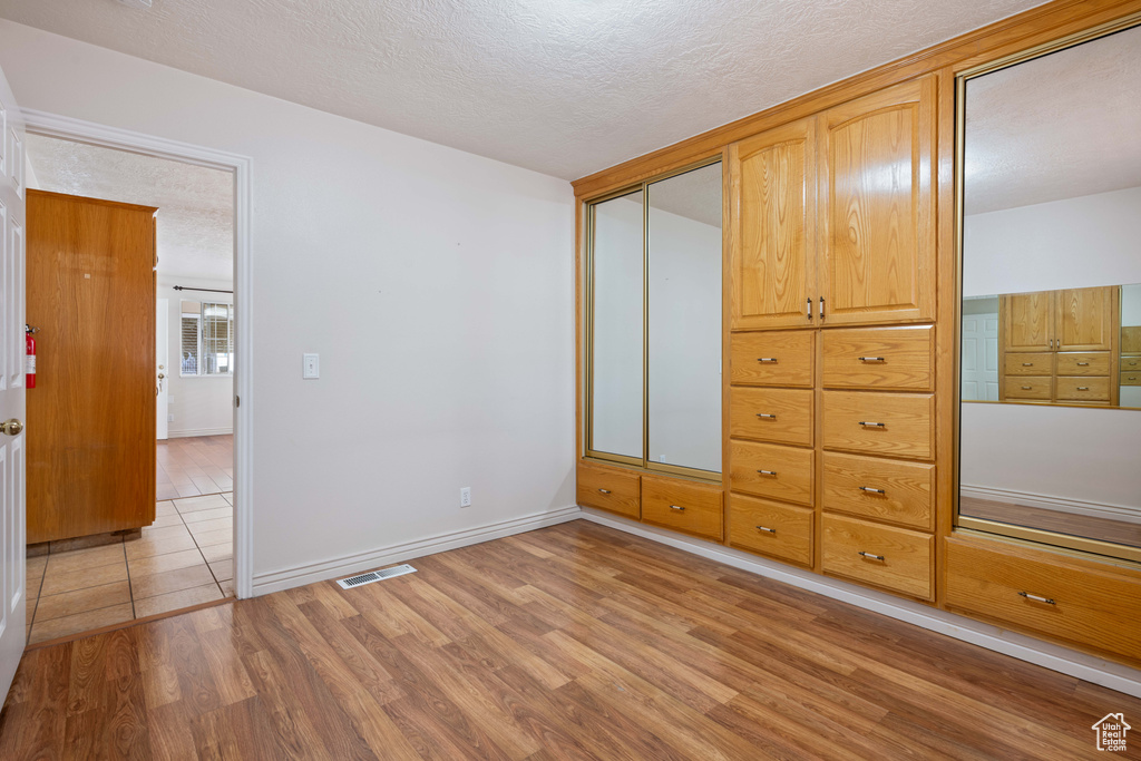 Unfurnished bedroom featuring a textured ceiling, light wood-type flooring, and a closet