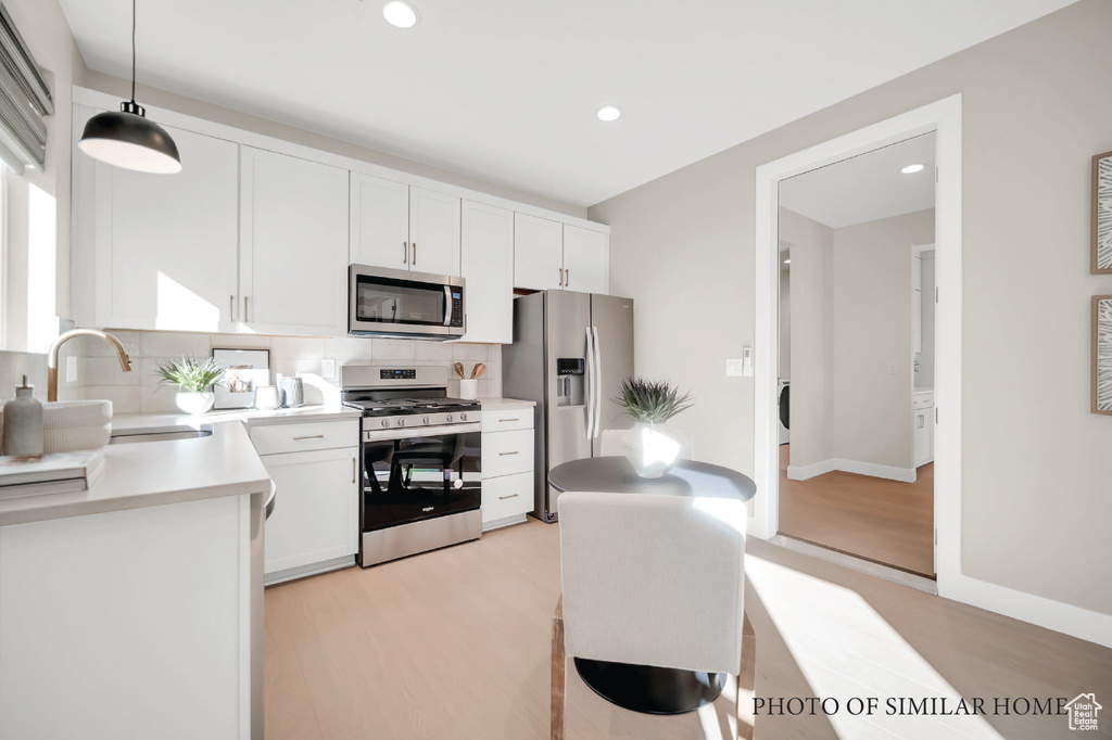 Kitchen with appliances with stainless steel finishes, decorative backsplash, white cabinets, pendant lighting, and light hardwood / wood-style flooring