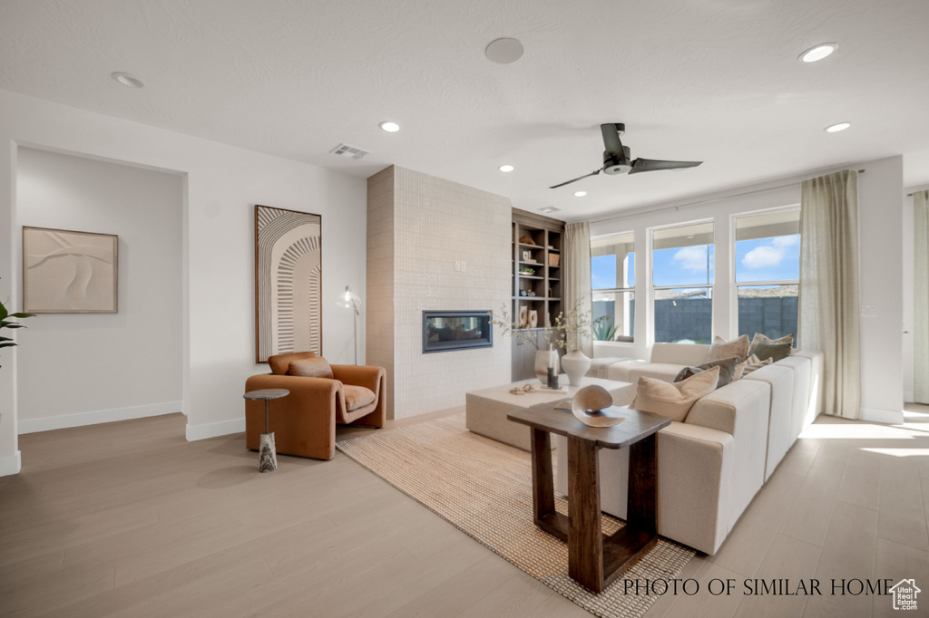 Living room featuring a fireplace, brick wall, ceiling fan, and light wood-type flooring