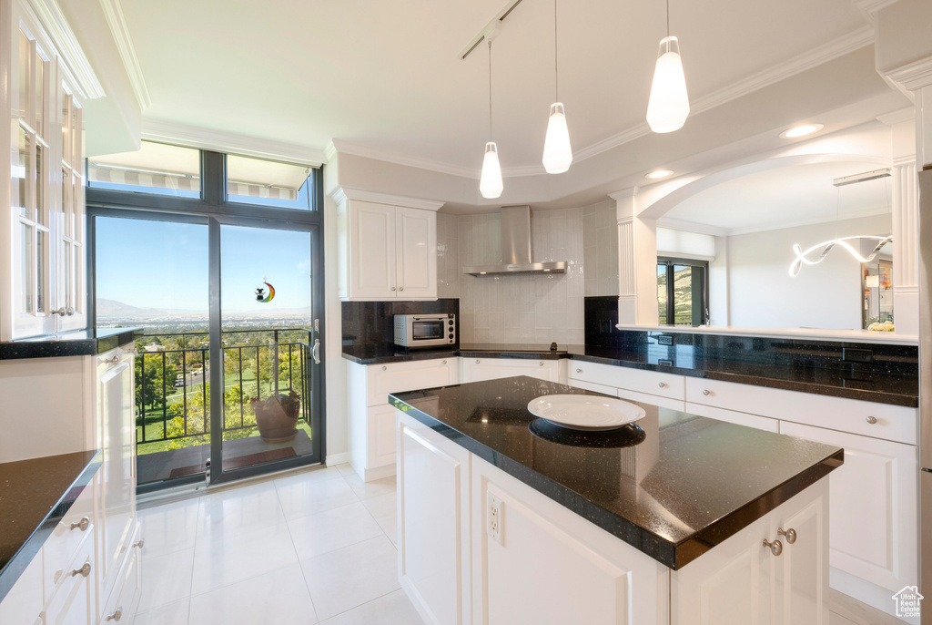 Kitchen with a center island, white cabinetry, hanging light fixtures, wall chimney exhaust hood, and decorative backsplash