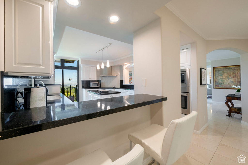 Kitchen with ornamental molding, kitchen peninsula, white cabinetry, and decorative light fixtures